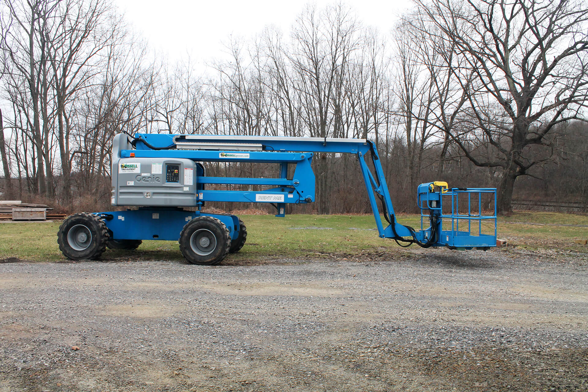 A partially extended, sixty foot articulating boom lift is standing in front of some trees. 